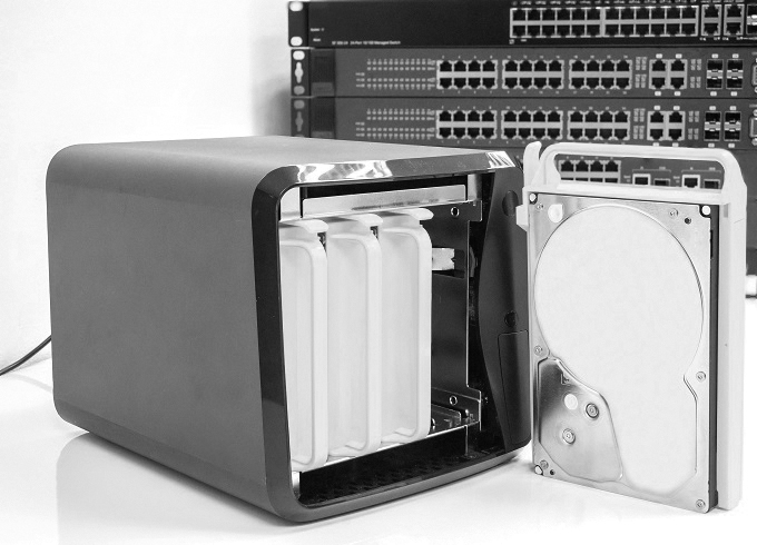 A photograph of a Network-attached storage (NAS) device is shown. The front of the device is opened to reveal the components inside.