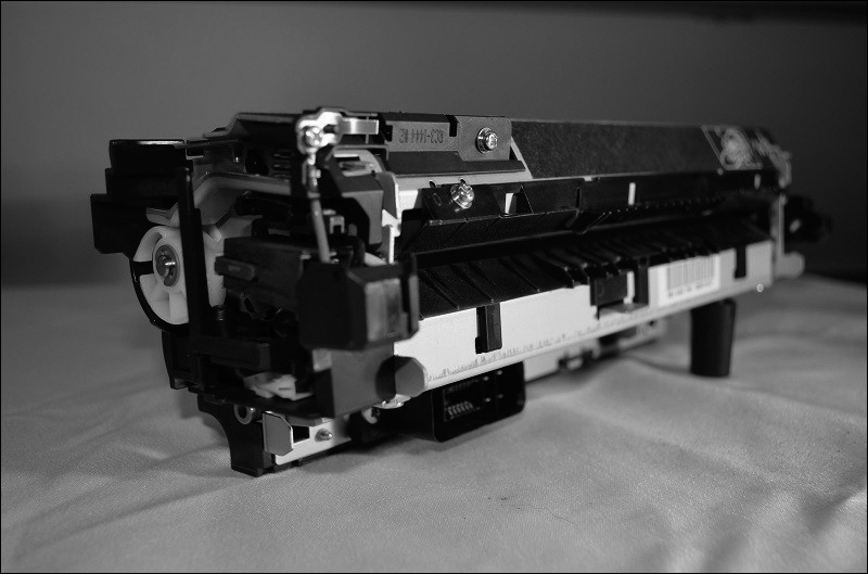 A photograph of the fuser assembly unit of the laser printer is shown. The fuser assembly unit includes rollers on the sides.