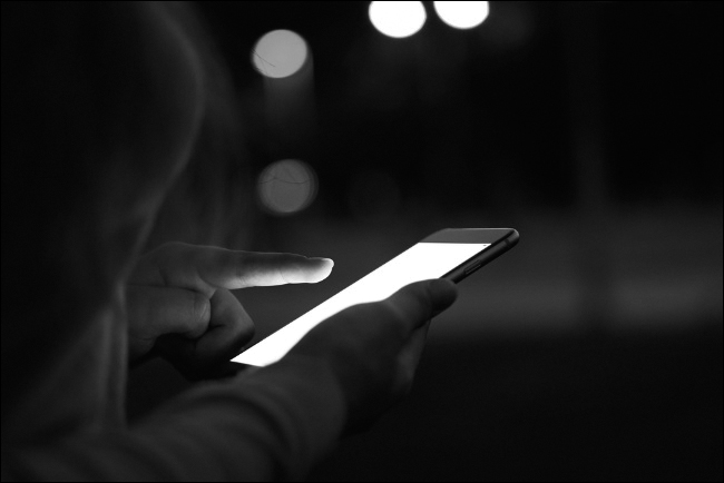 Photograph shows a very bright hand-held mobile device, in a dark surrounding.