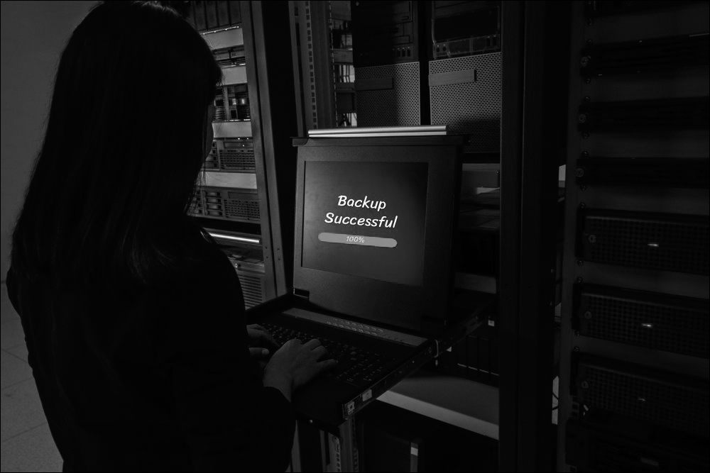 A photograph shows a female working inside a server room. The monitor displays the message, "backup successful."