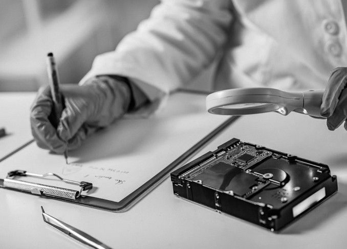 A photograph shows a forensic expert examining the hard drive through the magnifying glass and writing those data on the paper.