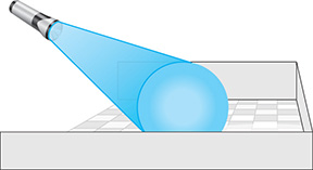 A flashlight shines a beam on a floor at an angle. The beam widens toward its end relative to where it first leaves the flashlight.