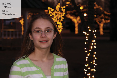 Night Portrait mode uses a slower shutter speed, higher ISO, and larger aperture to balance the background lights with the flash exposure.