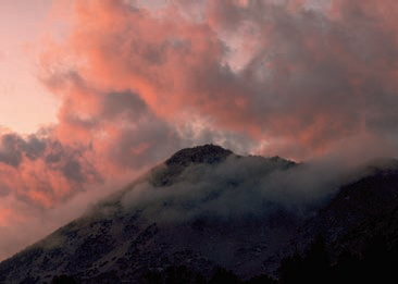 Sunrise lights the clouds near this mountain.