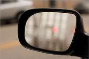 By focusing on the rearview mirror frame and using a wide f/2.8 aperture, both the reflected scene and the objects across the street are thrown out of focus.