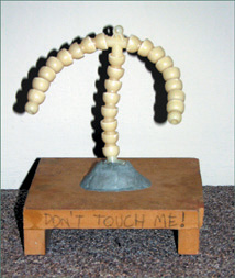 A plastic doll armature adhered to a wooden base.