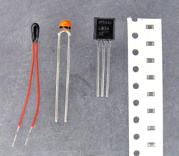 Various thermistors for measuring temperature. The first two are plain, the LM34 includes built-in electronics (center right), and the far right side shows a strip of tiny surface-mount thermistors.