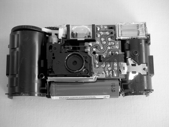 On the left is an open disposable camera. On this model, the big capacitor is tucked behind the flash (the flash is in the upper-right corner of the unit shown in the left picture). The right photo shows the back of the flash circuit; the AA battery gives a sense of how large that capacitor is—be careful! The two springy strips of copper on the left of the unit in the right photo (circled) form a rudimentary switch that triggers the flash. Remember this for later.