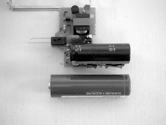 On the left is an open disposable camera. On this model, the big capacitor is tucked behind the flash (the flash is in the upper-right corner of the unit shown in the left picture). The right photo shows the back of the flash circuit; the AA battery gives a sense of how large that capacitor is—be careful! The two springy strips of copper on the left of the unit in the right photo (circled) form a rudimentary switch that triggers the flash. Remember this for later.