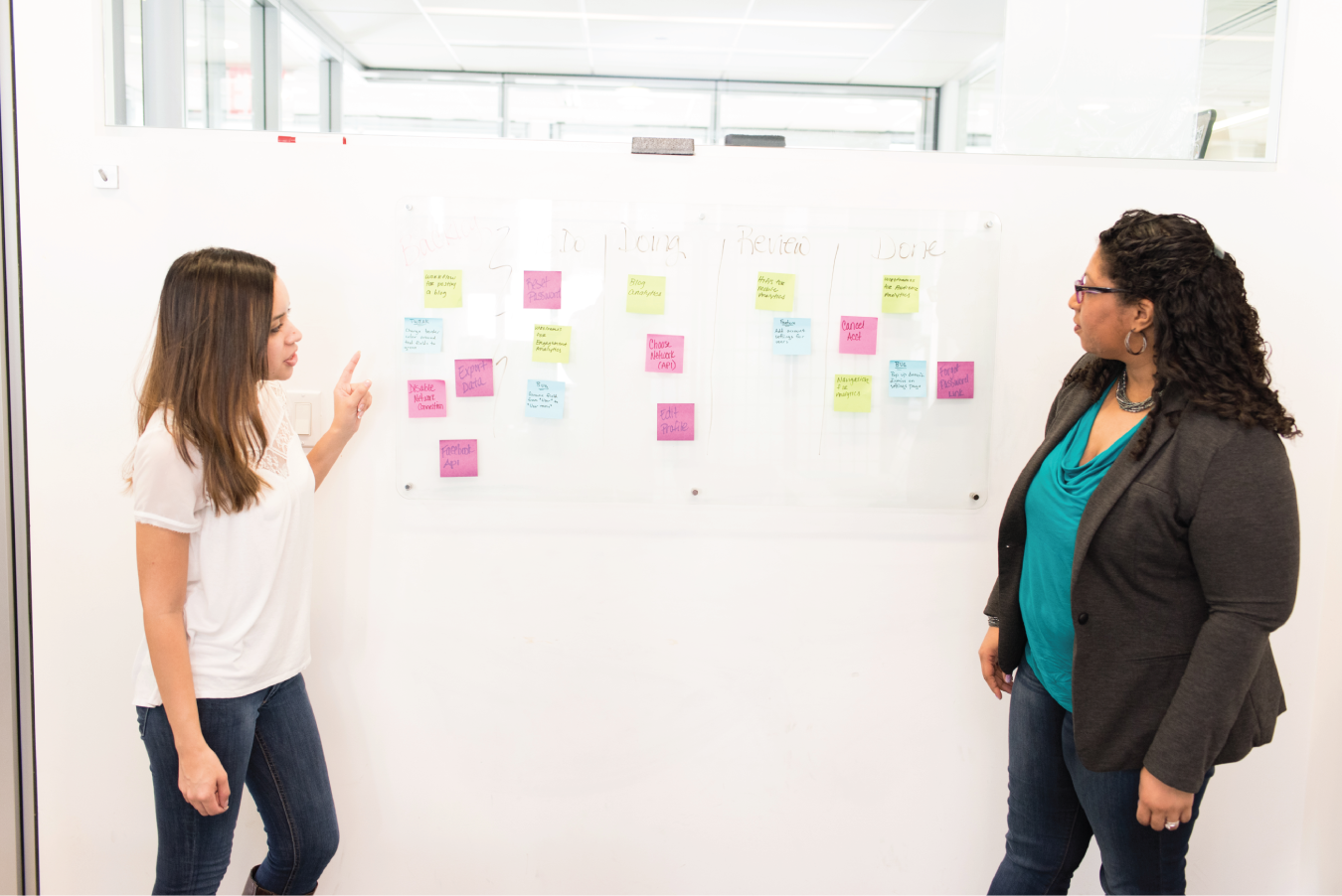 Photo depicts two women discussing near a board.