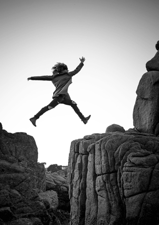 Image of a woman who is jumping from one cliff to another.