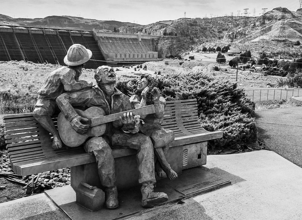 Photo depicts the Statue of famous American folk song writer Woody Guthrie in front of the Grand Coulee Dam on Columbia River in Washington State, USA.