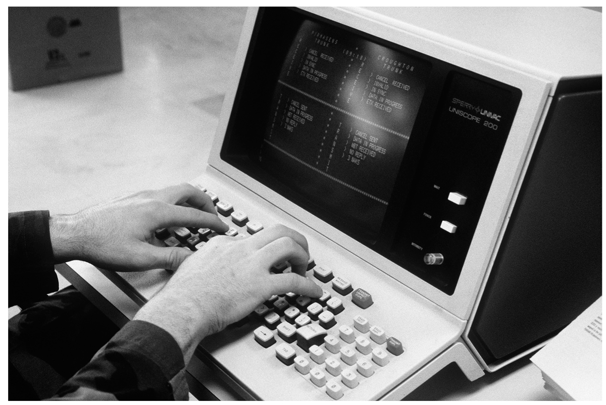 A photo shows a person’s hands typing on a keyboard attached to a box-like screen. A few push buttons and a regulator knob can be seen on the panel to the right of the screen.