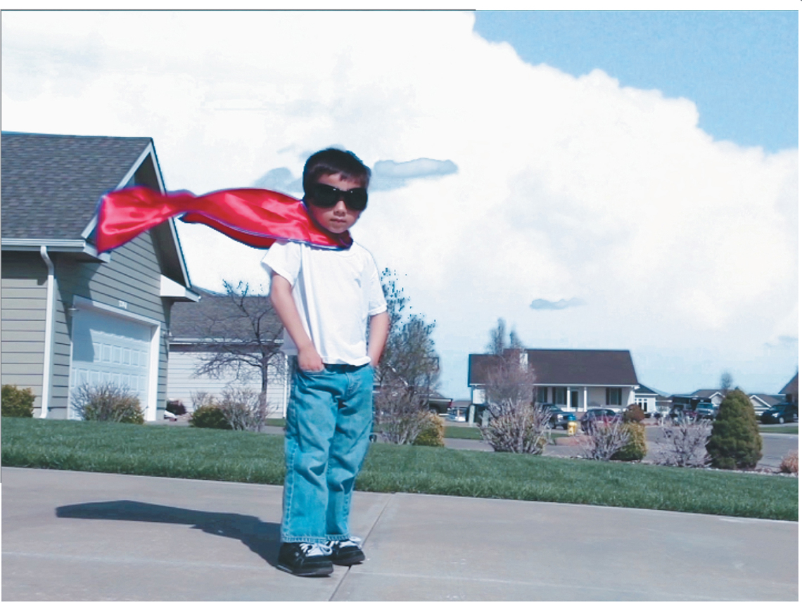 A composition window shows a clip of a young boy standing across a street. The boy poses with his hands inside his pant pockets. He wears a goggle and a superman cape over his shirt that flies with the wind.