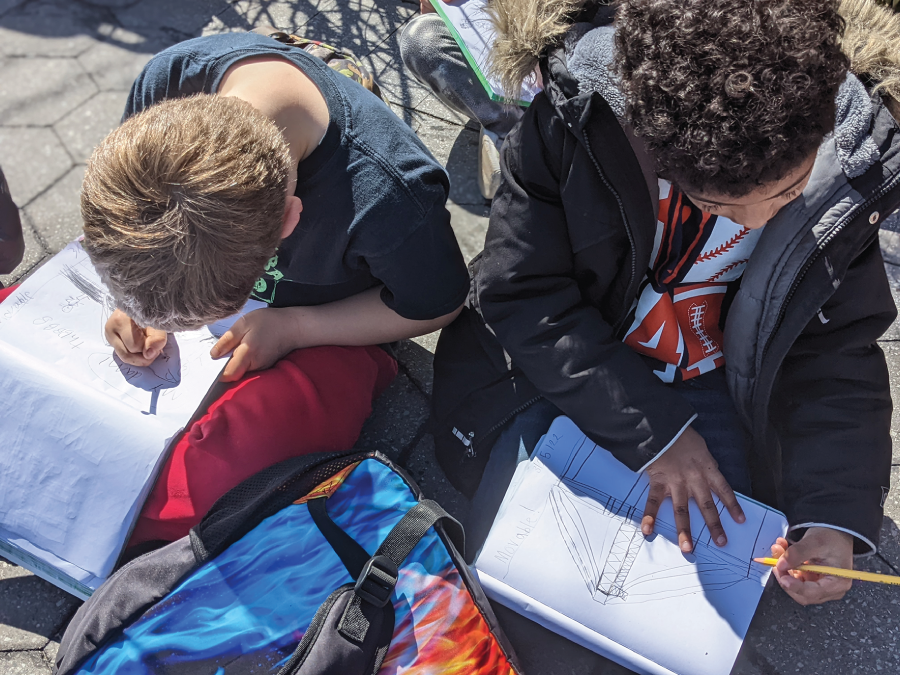 Photo depicts students drawing observations of a bridge in their notebooks.