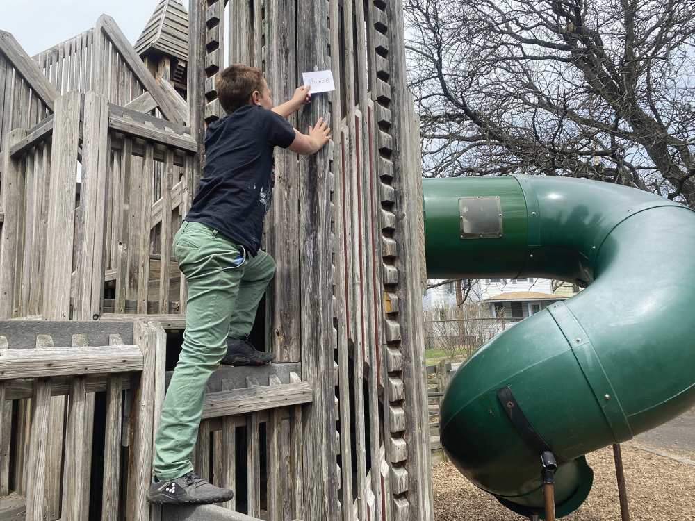 Photo depicts an older student hiding words on the playground for a younger class.