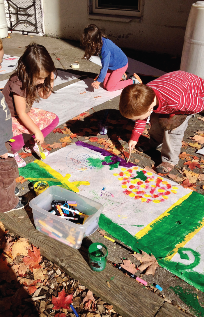 Photo depicts students painting scenes from a story outdoors.